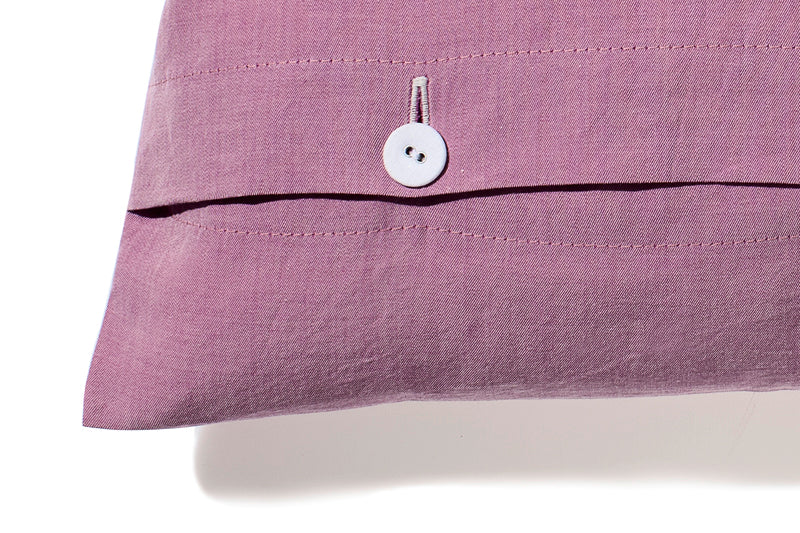 Bettwäsche Stonewashed Denim Pink: Hochwertiger Kissenbezug aus stonewashed Denim-Baumwolle in sanftem Rosa mit weißem Knopfverschluss, der einen lässigen, verwaschenen Look im Jeans-Stil zeigt. Detail des Bezugs mit charakteristischer Naht und funktionalem Verschlusssystem.