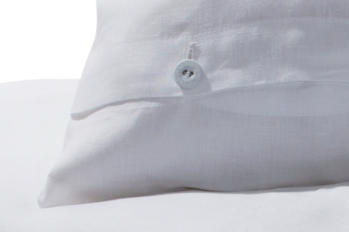 Hochwertige Bettwäsche Reines Leinen weiß mit eleganter Knopfleiste, Detail des Kissenbezugs zeigt gezwirnte Wäscheknöpfe in hellem Grau auf reinem weißen Leinen, italienische Qualitätswebung mit charakteristischer Leinenstruktur.
