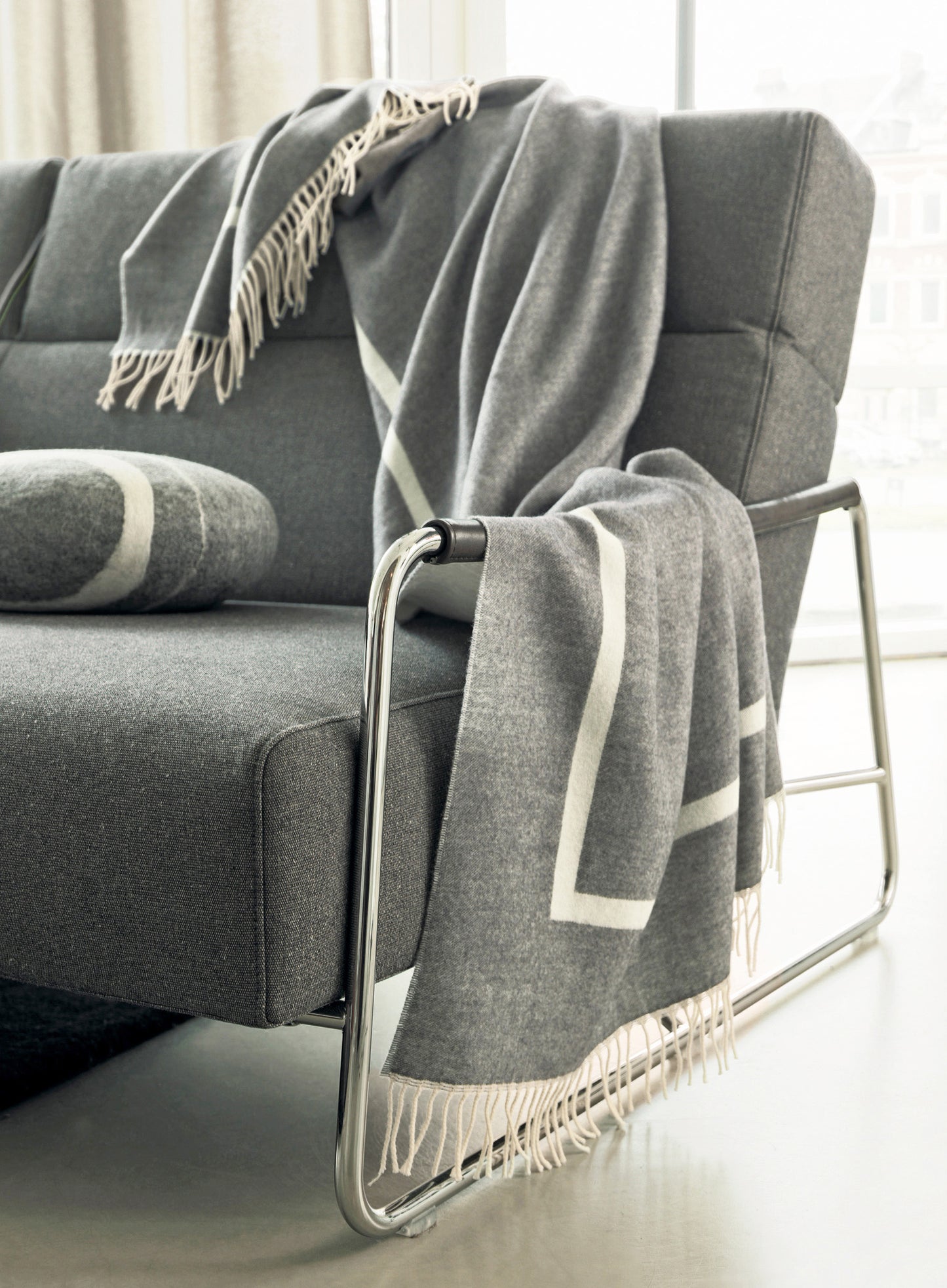 Luxuriöse FRANZ BARTH Kaschmir-Wolldecke Sylt in elegantem Grau mit cremefarbenen Fransen, stilvoll drapiert über einem modernen Sofa. Die hochwertige Decke aus 60% Kaschmir und 40% Wolle zeigt zeitlose bayerische Handwerkskunst. Wolldecken, Hersteller: Franz Barth