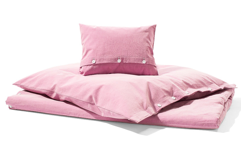Bettwäsche Stonewashed Denim Pink: Hochwertige Bettwäsche-Garnitur im Jeans-Look, stonewashed-Effekt in zartem Rosa. Kissenbezug mit stoffbezogenen Knöpfen auf weißem Hintergrund präsentiert. Lässiger, pflegeleichter Look aus 100% Baumwolle für zeitgemäßen Schlafkomfort.
