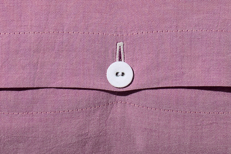 Bettwäsche Stonewashed Denim Pink: Detailaufnahme des stoffbezogenen weißen Wäscheknopfs auf rosa Denim-Stoff mit charakteristischer Jeans-Naht. Hochwertige Verarbeitung im stonewashed Look für einen lässigen, weichen Stil.