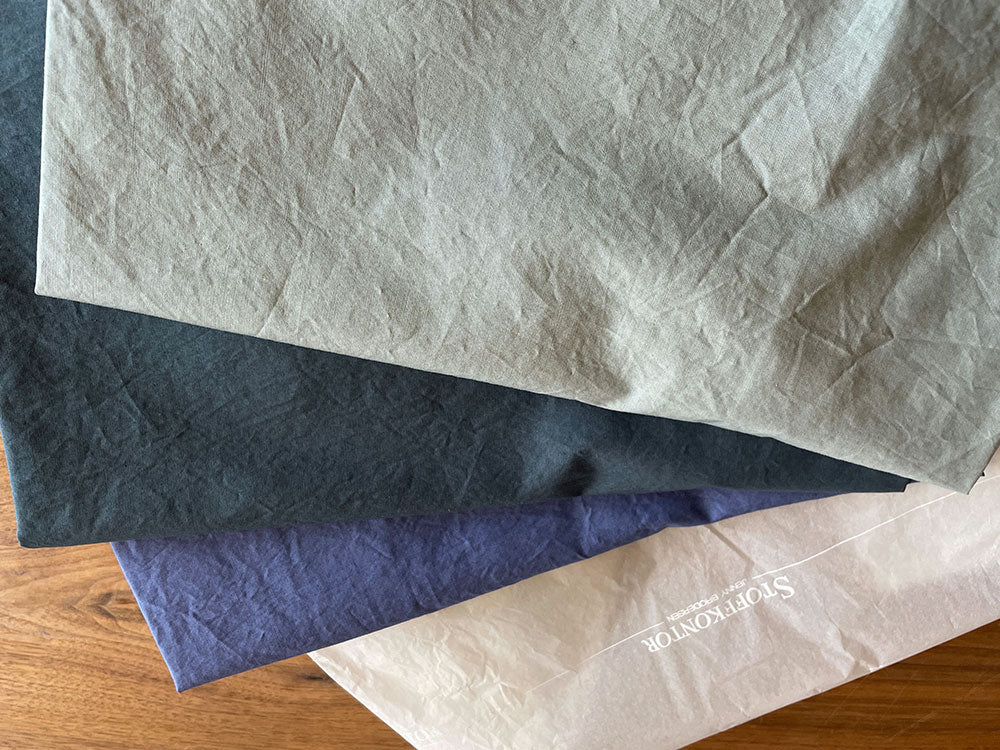 Bettwäsche Meeresschaum Gewaschene Baumwolle: Hochwertige Bettwäsche in verschiedenen Farbtönen auf Holzuntergrund - naturliche Knitteroptik zeigt die charakteristische Textur der gewaschenen Baumwolle. Moderne Farbpalette von Beige, Marineblau und Anthrazit für zeitloses Schlafzimmerdesign.