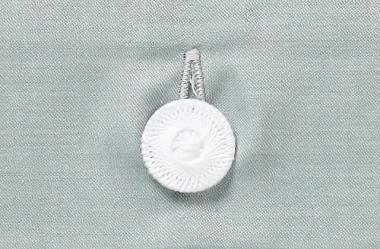 Bettwäsche Alice Damast - Hochwertiger weißer Knopf mit dekorativer Prägung auf elegant graugrünem Damastgewebe, Detail der verdeckten Knopfleiste. Exklusive italienische Webarbeit für Premium-Bettwäsche.
