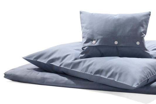Bettwäsche Amalfi Damast: Hochwertige Bettwäsche in elegantem Mittelblau, meliert gewebt mit weißem Kettfaden. Luxuriöse Satinbindung mit verdeckter Knopfleiste und gezwirnten Wäscheknöpfen. Kissen und Bettdeckenbezug in harmonischer Komposition auf weißem Hintergrund.