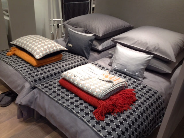 Bettwäsche Caviar Nadelstreifen Damast: Elegantes Bettenset in Grau mit feinen Nadelstreifen, dekorativ arrangiert mit gemusterten Kissen und Decken in Orange, Rot und Grautönen auf einem Bett. Die hochwertige Damast-Bettwäsche zeigt verschiedene Texturen und Muster in harmonischer Kombination.