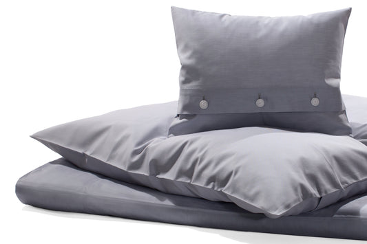 Bettwäsche Perla Damast: Elegante hellblaue Bettwäsche aus hochwertigem italienischem Damast mit weißem Kettfaden, dekorativen Knöpfen und verdeckter Knopfleiste. Kissenbezüge und Bettdeckenbezug in harmonischer Anordnung präsentiert.
