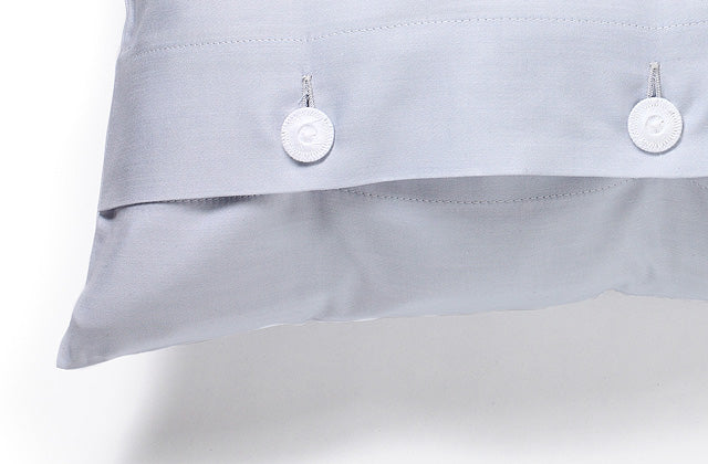 Bettwäsche Perla Damast: Elegantes Kissen in zartem Hellblau mit weißen Knöpfen, hochwertige Damastwebung mit verdeckter Knopfleiste. Detail der Kissenhülle zeigt die feine Satinbindung und exklusive italienische Verarbeitung.