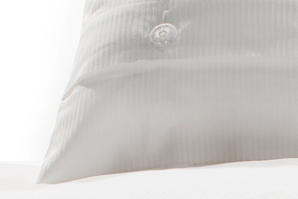 Elegante Bettwäsche Weiß Feinstreifen Damast mit dezent eingearbeitetem Streifenmuster, hochwertig verarbeitet. Kissen mit feinem Logo-Detail zeigt die Premium-Qualität des italienischen Damastgewebes in strahlendem Weiß.