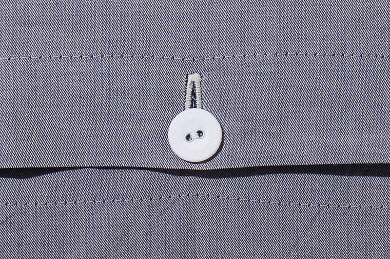 Detailaufnahme eines weißen Knopfes der Bettwäsche Bluette Damast, eingenäht in hochwertigen blauen Damast-Stoff mit eleganter Nahtführung. Zeigt die hochwertige Verarbeitung und den Qualitätsstandard der Bettwäsche.