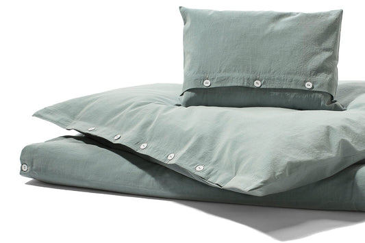 Bettwäsche Stonewashed Denim Jade: Hochwertige Bettwäsche in sanftem Jadegrün mit charakteristischer Stonewashed-Optik, stoffbezogenen Knöpfen und lässigem Denim-Look. Fotografiert in natürlichem Licht, zeigt Kissenbezug und Bettdeckenbezug in entspannter Präsentation.