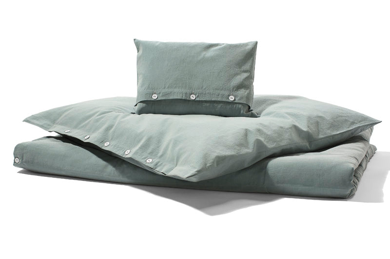 Bettwäsche Stonewashed Denim Jade - Hochwertige Baumwoll-Bettwäsche in pudrigem Jadegrün mit Stonewashed-Effekt, lässigem Denim-Look und stoffbezogenen Knöpfen, fotografiert in natürlicher Beleuchtung mit gestapelten Kissen und Bettdecke.