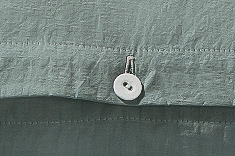 Bettwäsche Stonewashed Denim Jade - Detailaufnahme des hochwertigen stoffbezogenen Wäscheknopfs auf dem jadegrünen, stonewashed Baumwollstoff. Die charakteristische Denim-Textur und der weiche, pudrige Farbton sind deutlich erkennbar. Home page, Alle Bettwäschen, Denim-Style-Bettwäsche, Unifarbene Bettwäsche, Hersteller: Stoffkontor
