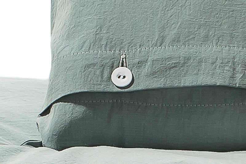 Detailaufnahme der Bettwäsche Stonewashed Denim Jade mit stoffbezogenem Knopfverschluss. Die jadegrüne Baumwollbettwäsche zeigt die charakteristische Stonewashed-Optik mit weicher, matter Oberfläche und hochwertiger Nahtverarbeitung.