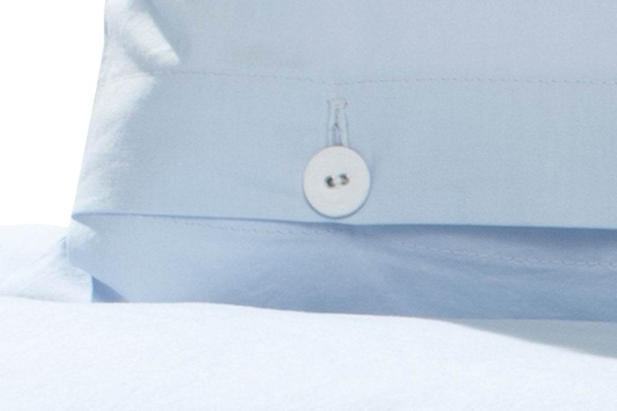Detailaufnahme der Bettwäsche Arctic hellblau mit hochwertiger Knopfleiste aus gezwirnten Wäscheknöpfen auf hellblauem, vorgewaschenem Baumwollstoff. Elegante Verarbeitung zeigt die Qualität der in Italien gewebten und in Deutschland gefertigten Bettwäsche.