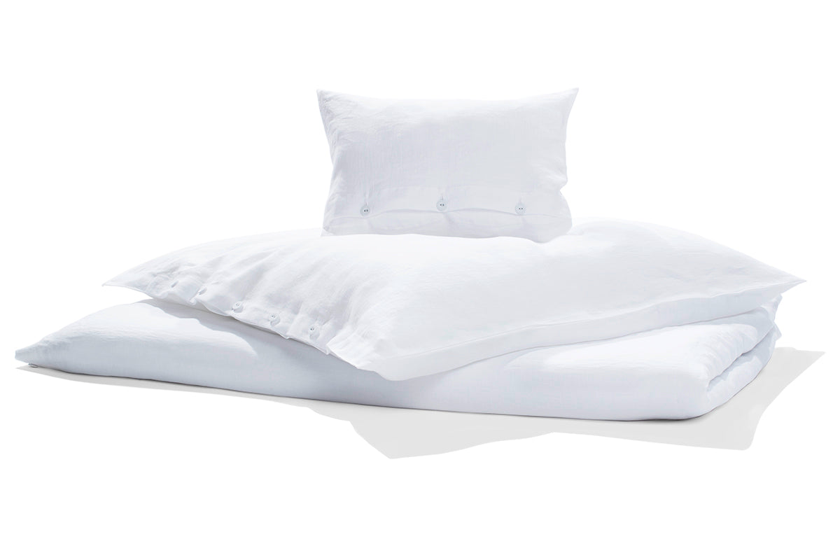 Bettwäsche Reines Leinen weiss, vorgewaschen GOTS: Hochwertige weisse Leinenbettwäsche mit Kissen und Bettbezug, elegant drapiert auf hellem Hintergrund. Vorgewaschenes, weiches Material mit natürlicher Struktur und klassischer Knopfleiste. GOTS-zertifizierte nachhaltige Qualität aus italienischer Weberei.