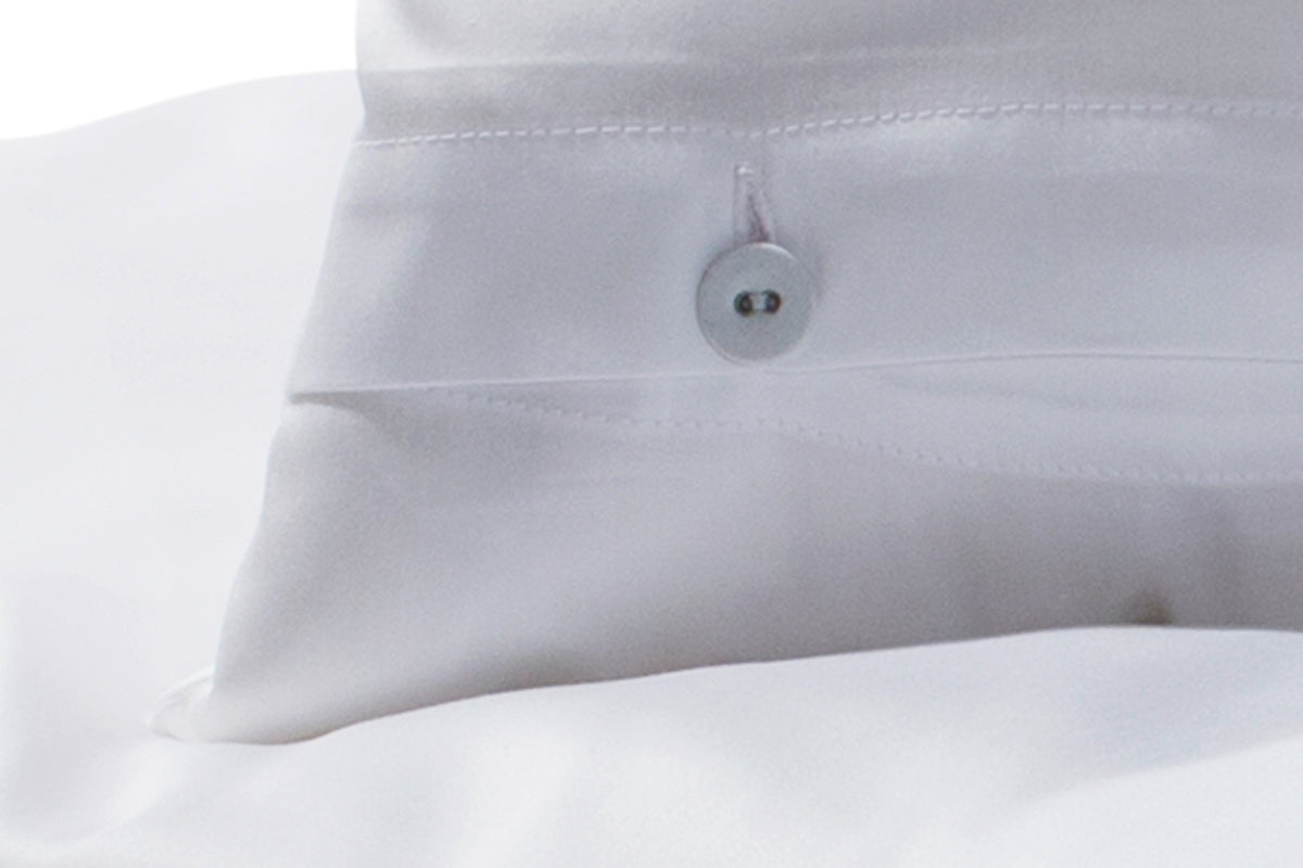 Hochwertige Bettwäsche Mako-Satin weiss mit eleganter Knopfleiste, Detail der stoffbezogenen Wäscheknöpfe auf glänzender, weißer Satinoberfläche. Exklusiv in Italien gefertigt für Stoffkontor.
