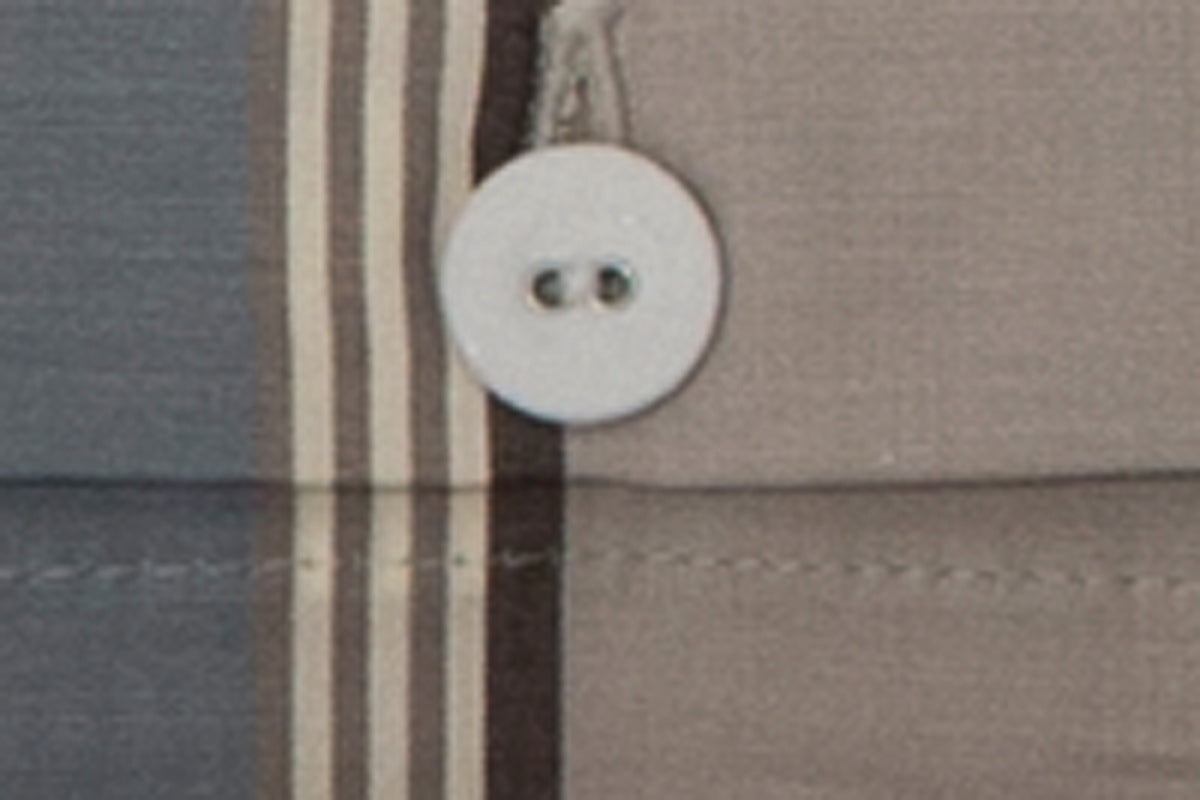 Bettwäsche Breiter Streifen Nordisch by Nature - Detailaufnahme eines weißen Knopfes auf gestreiftem Baumwollstoff in Beige- und Brauntönen. Die hochwertige Stoffqualität und klassische Knopfleiste sind deutlich erkennbar.