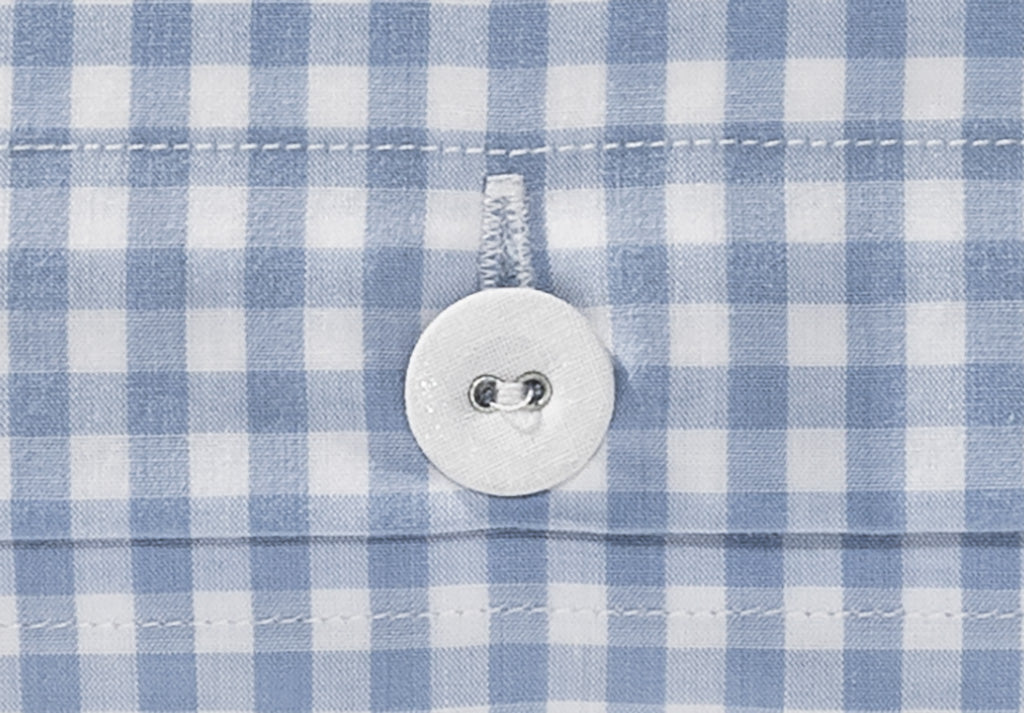 Bettwäsche Nordisch by Nature Vichy Karo Hellblau: Detailaufnahme eines weißen Knopfes auf hellblauem Vichy-Karomuster. Der Stoffbezogene Knopf ist sorgfältig auf dem Baumwollstoff angenäht, umgeben von präzisen Karovierkanten in Hellblau und Weiß.