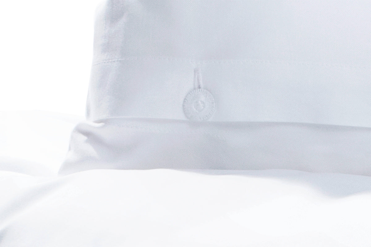 Bettwäsche Oxford, Weiss - Detailaufnahme des eleganten gezwirnten Wäscheknopfs auf reinem weissem Baumwollstoff. Die hochwertige Verarbeitung zeigt sich in der klaren Struktur und klassischen Knopfleiste der exklusiven italienischen Webung.