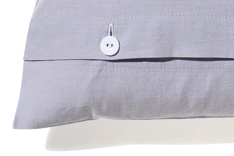 Detailaufnahme der Bettwäsche Stonewashed Denim Ciclamino in softem Grau-Lavendel mit hochwertigem weißem Stoffknopfverschluss, charakteristische Stonewashed-Optik und Denim-typische Webstruktur zeigend.