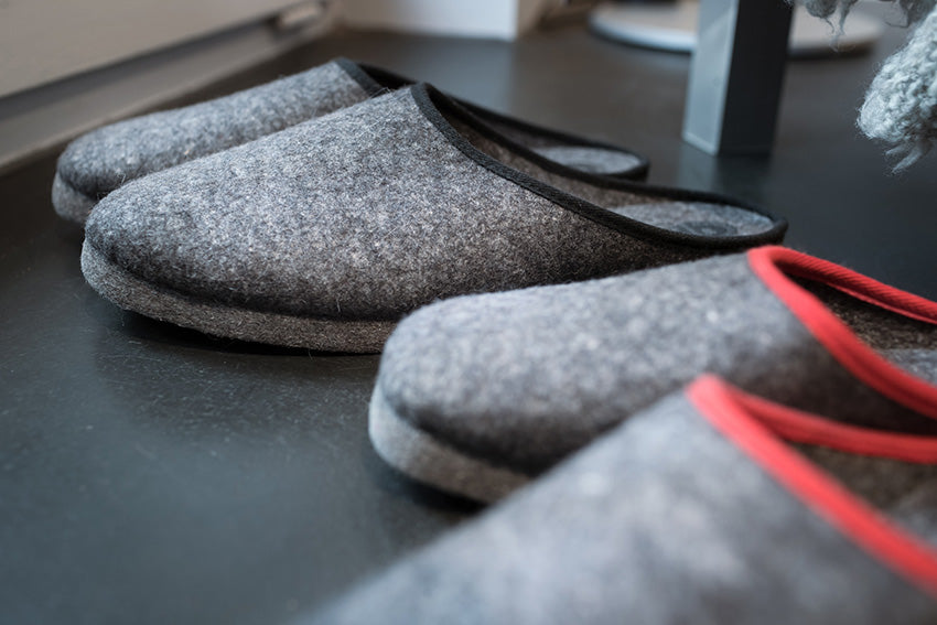 Handgefertigte graue Filzpantoffeln offen mit schwarzem Einfassband auf dunkler Oberflache fotografiert, zeigt die hochwertige Wollfilz-Verarbeitung und komfortable Passform. Traditionelle deutsche Handwerkskunst vom Stoffkontor. Filzpantoffeln offen, Band schwarz - Pantoffeln, Hersteller: Stoffkontor