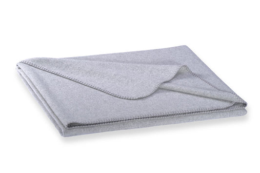 Hochwertige Steiner1888 Wolldecke Alina Marmor in elegantem Grau, gefertigt aus Alpaka- und Merinowolle. Die Decke ist kunstvoll gefaltet und zeigt eine dezente Kantenverzierung. Die weiche Textur der Premium-Wolldecke ist deutlich erkennbar. Wolldecken, Hersteller: Steiner 1888